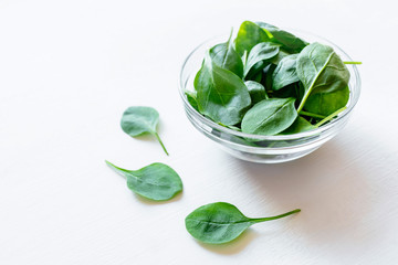 Fresh green spinach leaves in glass bowl on white table. Organic food, healthy diet, vegetarian food. Top view.