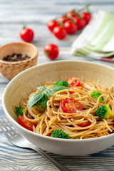 Whole wheat spaghetti pasta with broccoli, cherry tomatoes and basil in bowl on wooden background. Selective focus.