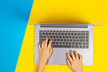 Kid hands typing on laptop computer keyboard, top view, yellow and blue background