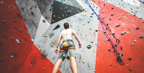 Sportsman climber is looking on steep rock, climbing on artificial wall indoors. Extreme sports and...