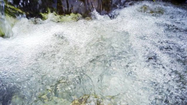 Close up of water stream with white and transparent bubbles. Slow motion.