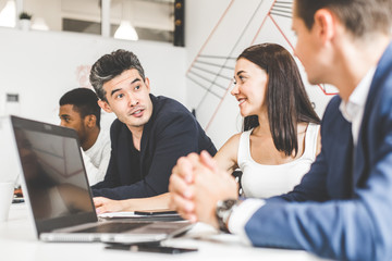 A team of young office workers, businessmen with laptop working at the table, communicating together in an office. Corporate businessteam and manager in a meeting. coworking.