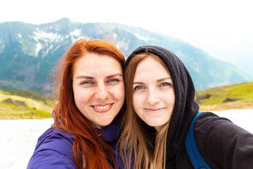 Two girls take a picture with their mobile. Two friends enjoy nature and the outdoors on the side of the mountain