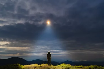 Gordijnen De UFO schijnt op een mannetje dat op de berg staat © Artem