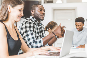 Obraz premium A team of young office workers, businessmen with laptop working at the table, communicating together in an office. Corporate businessteam and manager in a meeting. coworking.