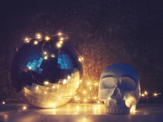 A decorative figure in the form of a blue human skull and a large disco ball are on a cement background with cracks and scuffs. A garland shines around the skull and ball.