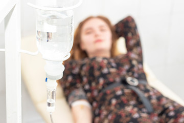 Closeup of saline drip with background Woman patient on the bed get better, when they come for treatment in room hospital. concept healthcare and medicine