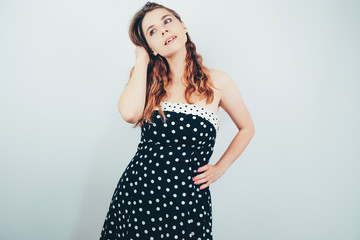 Pretty girl in  black retro dress with white polka dots  dreamily looking aside. Attractive young  european woman with ombre wavy hair on grey background.