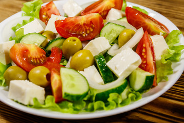 Greek salad with fresh vegetables, feta cheese and green olives on wooden table