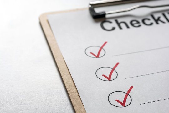 Abgehakte Checkliste auf einem Klemmbrett liegt auf einem hellen Schreibtisch
