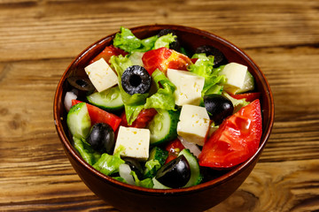 Greek salad with fresh vegetables, feta cheese and black olives on wooden table