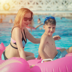 Swimming with pink rubber floater. Mother and boy on summer vacation.