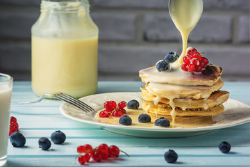 Tasty breakfast with blueberries and currants. Condensed milk is pouring onto pancakes. Delicious...