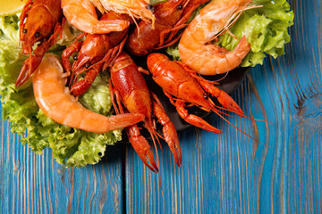 Boiled crayfish and shrimps with green salad and lemon slices on a plate, top view