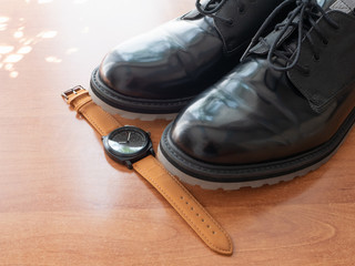 pair of man black glossy formal shoes and wrist watches on wooden desk