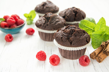 Chocolate muffins with raspberries and mint leaves on white table