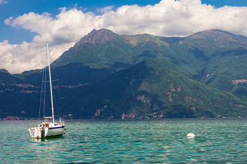 View to sailboat anchored in harbor the village of Varenna on Lake Como. Scenic landscape on background alps mountains, trees and water. Milan Province of Lecco. Italian region Lombardy, Italy Europe