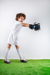 Fototapeta na wymiar Boy with soccer ball on the green grass.Excited little toddler boy playing football on soccer field against light background. Active childhood and sports passion concept. Save space