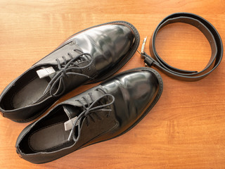 pair of elegant glossy black formal man shoes and leather belt on wooden table