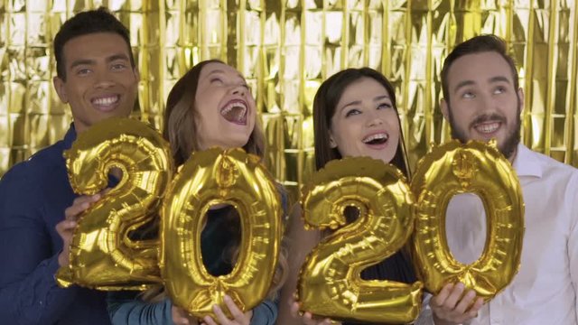 2020 year. falling golden confetti .4 people with golden letters made of foil are dancing on a gold background. Slow motion