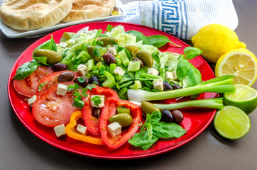 A horizontal shot of a traditional Greek salad with olives feta cheese fresh tomatoes greens and pita bread. 