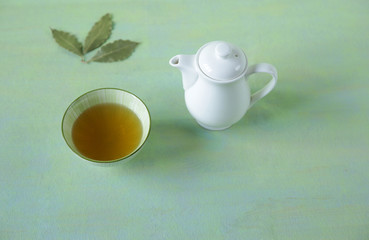 green tea in a bowl with a teapot and tea leaves on a light green surface. It is a rich source of antioxidants and polyphenols. A healthy drink for health and vitality.