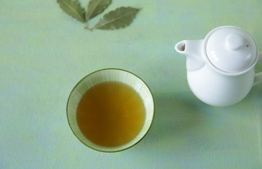 Flat lay green tea in a bowl with a teapot and tea leaves on a light green surface. It is a rich source of antioxidants and polyphenols. A healthy drink for health and vitality.