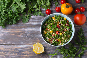 Oriental salad tabbouleh with cabbage kale, parsley, bulgur, tomatoes and red onions on a wooden table, top view. healthy homemade food
