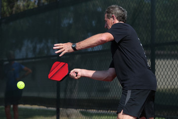 A senior athlete hits a shot, competing in singles, of a pickleball tournament.