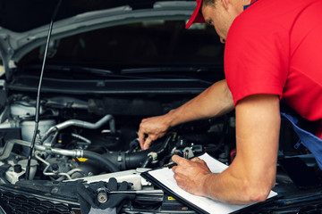 Fototapeta na wymiar car maintenance - mechanic check the engine and writing in checklist