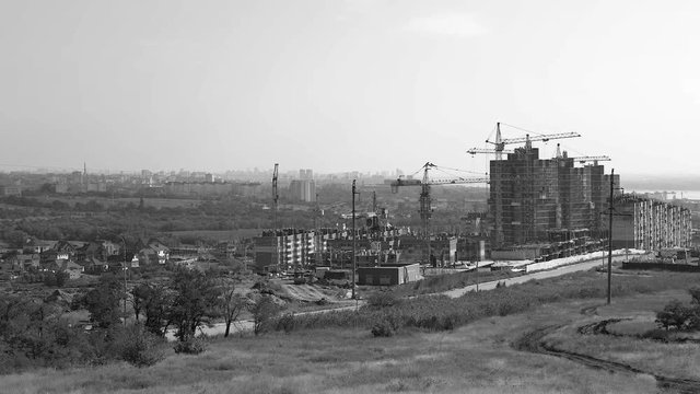 Several tower cranes build a multi-storey building and move cargo, long-range plan, time-lapse, monochrome