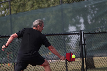 A senior athlete hits a shot, competing in singles, of a pickleball tournament.