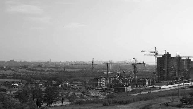 Several tower cranes build a multi-storey building and move cargo, long-range plan, time-lapse, monochrome