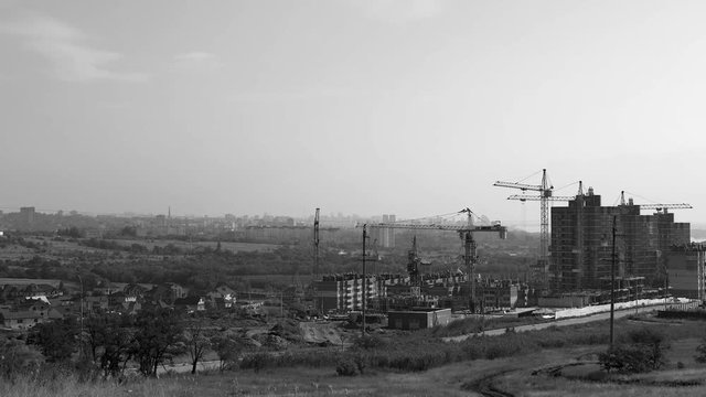 Several tower cranes build a multi-storey building and move cargo, long-range plan, time-lapse, monochrome