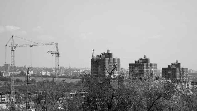 Several tower cranes build a multi-storey building and move cargo, long-range plan, time-lapse, monochrome