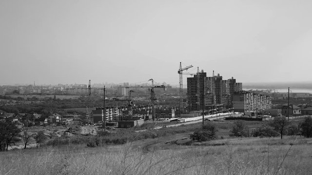 Several tower cranes build a multi-storey building and move cargo, long-range plan, time-lapse, monochrome