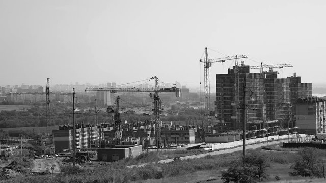 Several tower cranes build a multi-storey building and move cargo, long-range plan, time-lapse, monochrome