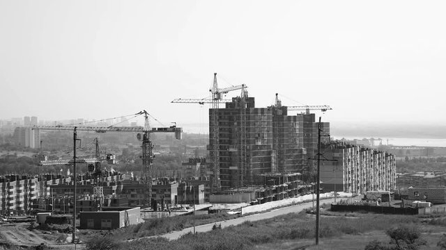 Several tower cranes build a multi-storey building and move cargo, long-range plan, time-lapse, monochrome