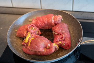 beef roulades, german stuffed meat rolls roast in a pan on the black stove