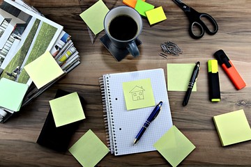 Sticky notes, scissors, magnifying glass, triangular ruler, pen, yellow and orange marker, smartphone, newspapers, coffee on office desk on wooden background
