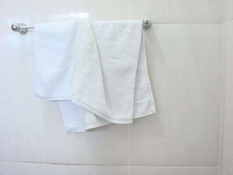 Toalha de rosto branca pendurada em banheiro branco.