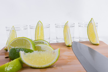 Close-up of lemon slices lined with tequila cups and a knife on a wooden cutting board insulated on...