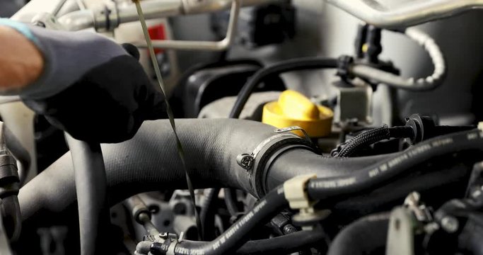 mechanic in garage doing car engine oil change and level inspection