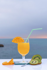 Colorful photo of orange juice in a glass, two slices of ripe orange and three slices of green kiwi with sea bottom - Fresh and ripe orange - Green kiwi with seeds