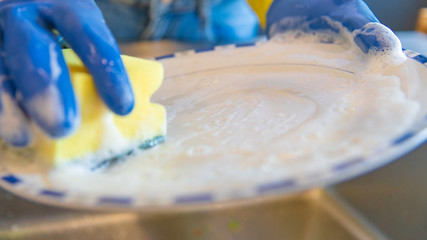 Close-up of hands with gloves and sponge washing dishes in kitchen sink