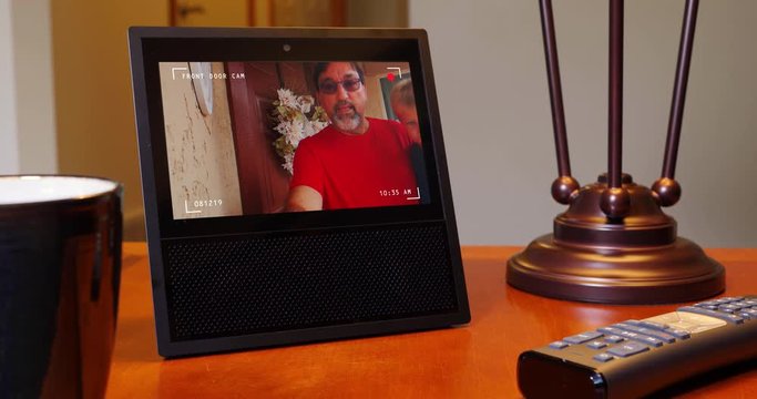 A personal assistant on a living room end table shows the time then the front door camera view where a grandfather holding his grandson is waiting.	 	