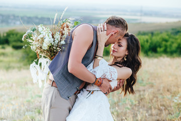 The groom dressed in the style of boho gently kisses the bride.
