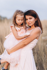 Mother and daughter look at the sea in pink dresses on the Sunset. 