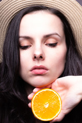 young woman with a hat on her head is holding an orange