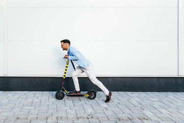 Young modern man using and driving electric scooter on city street. Modern and ecological transportation concept.